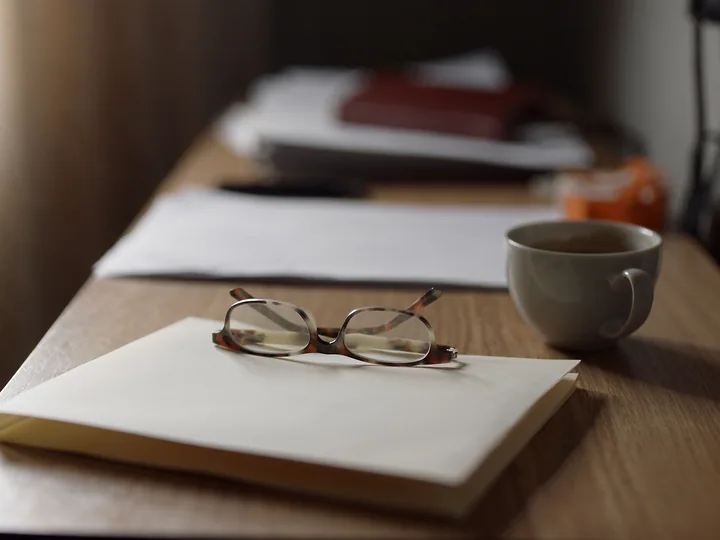 Reading glasses on a closed manila folder beside a cup of coffee