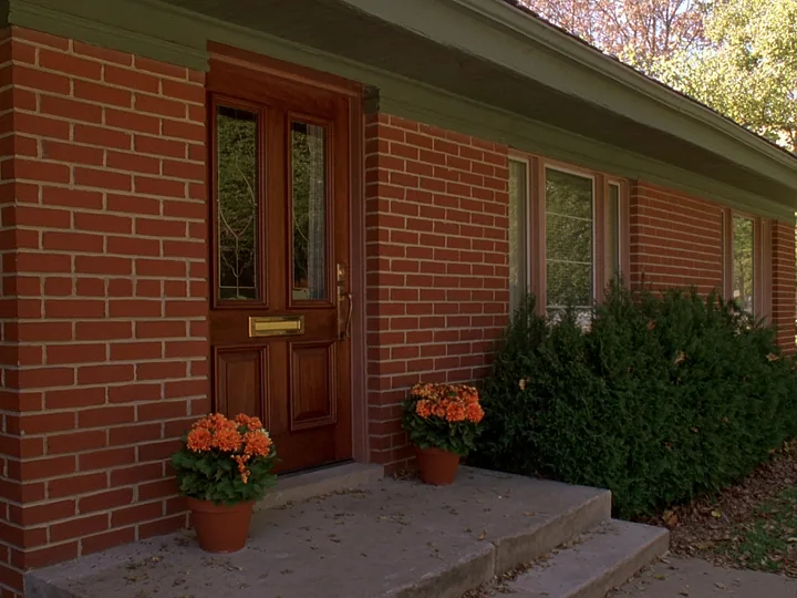 A brick front step and a wooden door with two pots of orange mums