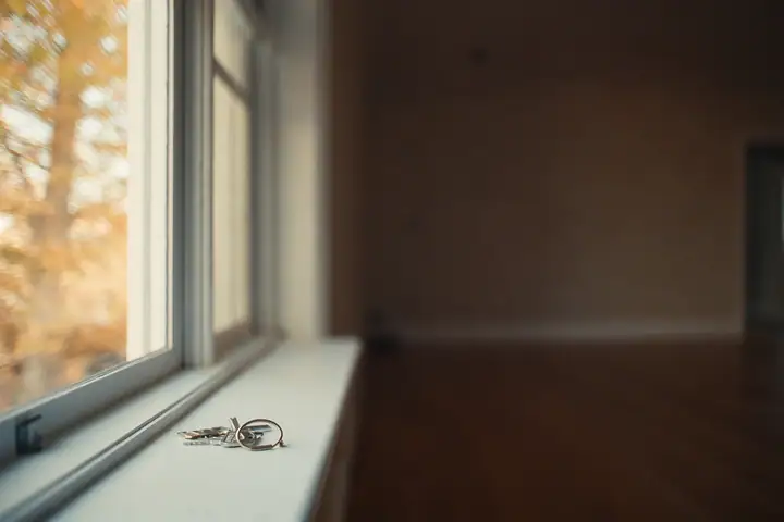 A ring of house keys on a sunlit windowsill, an empty room behind it and an autumn tree outside
