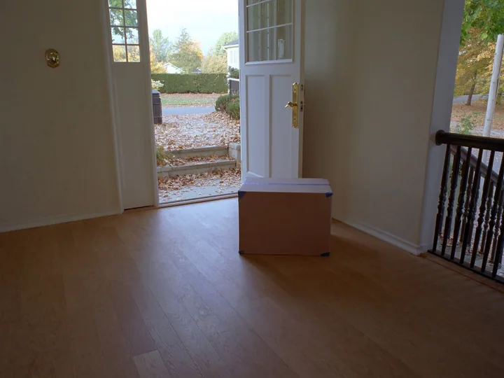 A taped moving box inside an open front door, autumn leaves on the steps outside