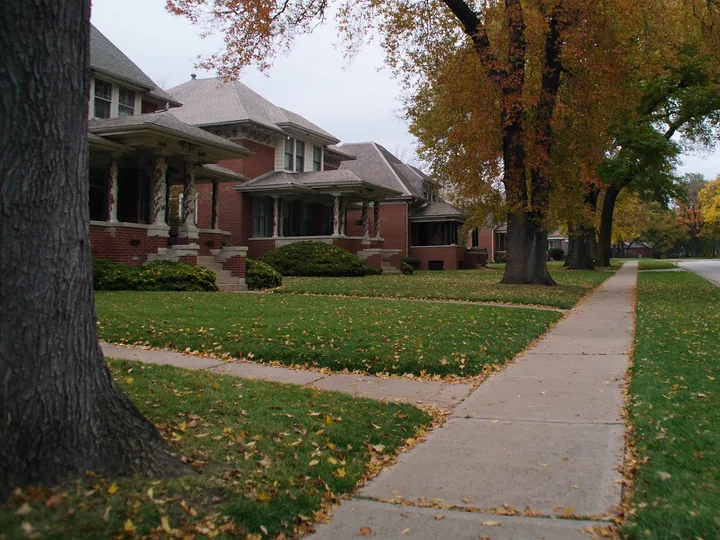 Brick bungalows and a tall autumn tree along a quiet sidewalk